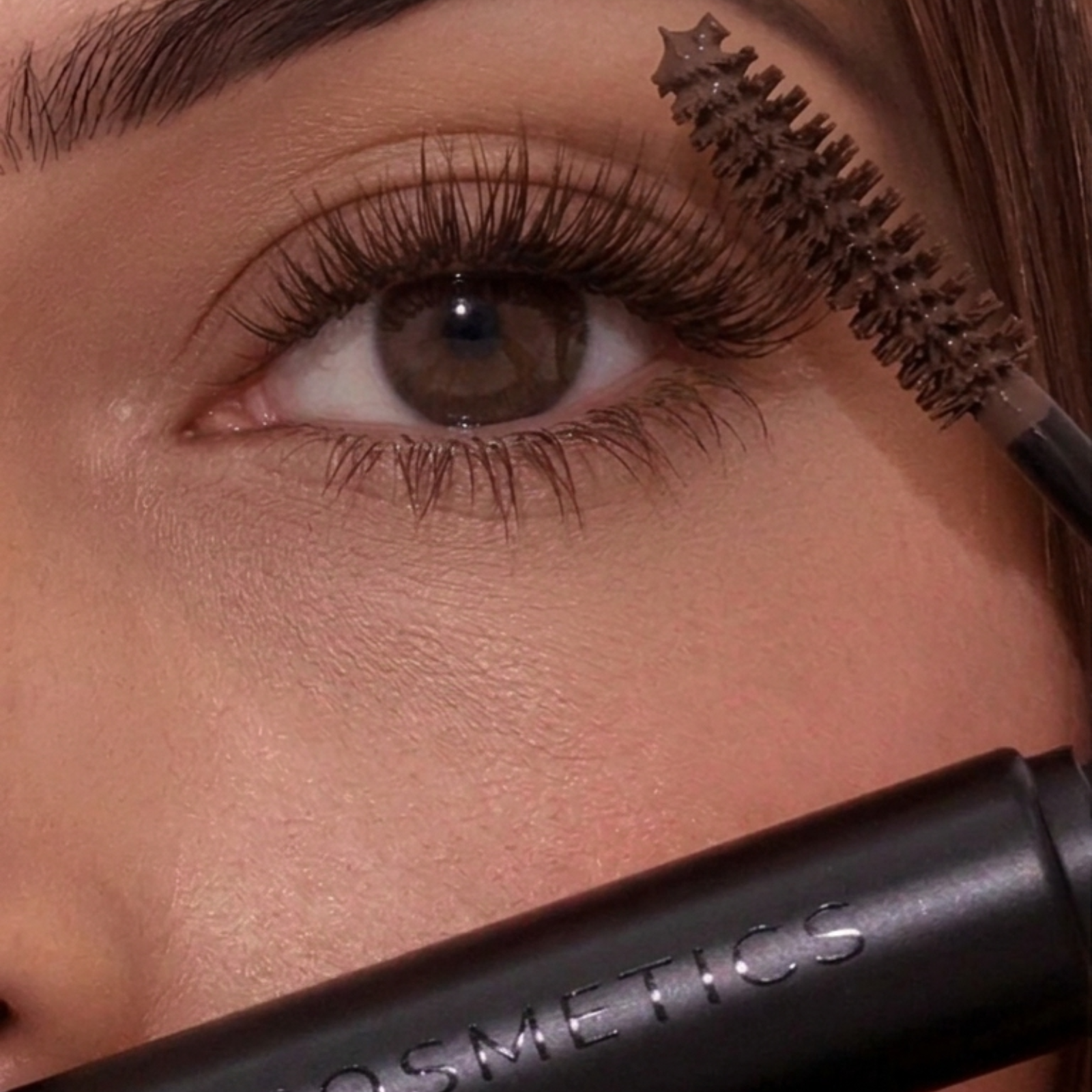 Close-up of a person applying makeup with a brush near their eye, featuring a brand name.