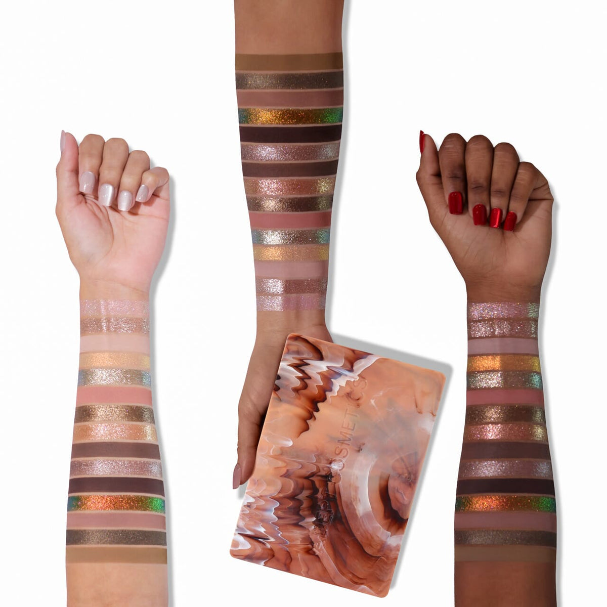Three human arms and hands are shown against a white background, each with horizontal swatches of shimmering makeup or pigment bands applied along the forearms. A rectangular palette or book-like object with an abstract marbled peach, pink, and brown cover is held in the center.